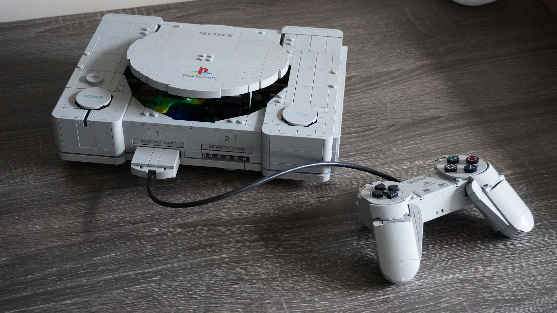 LEGO model of a Sony PlayStation 1 console with a wired controller on a wooden table.