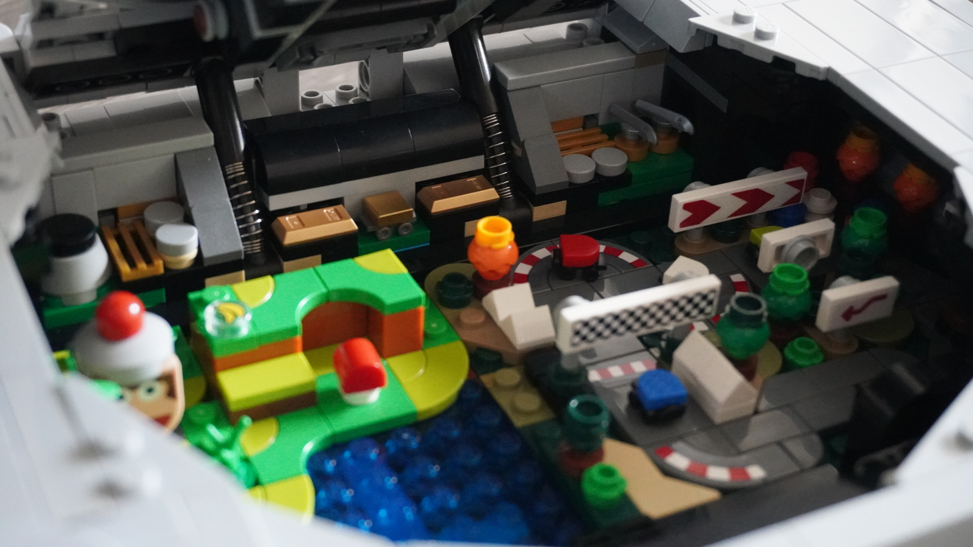 Interior of a LEGO diorama showing grey walls, machinery, and a bright green colorful platform with a blue stud-filled pool nearby.