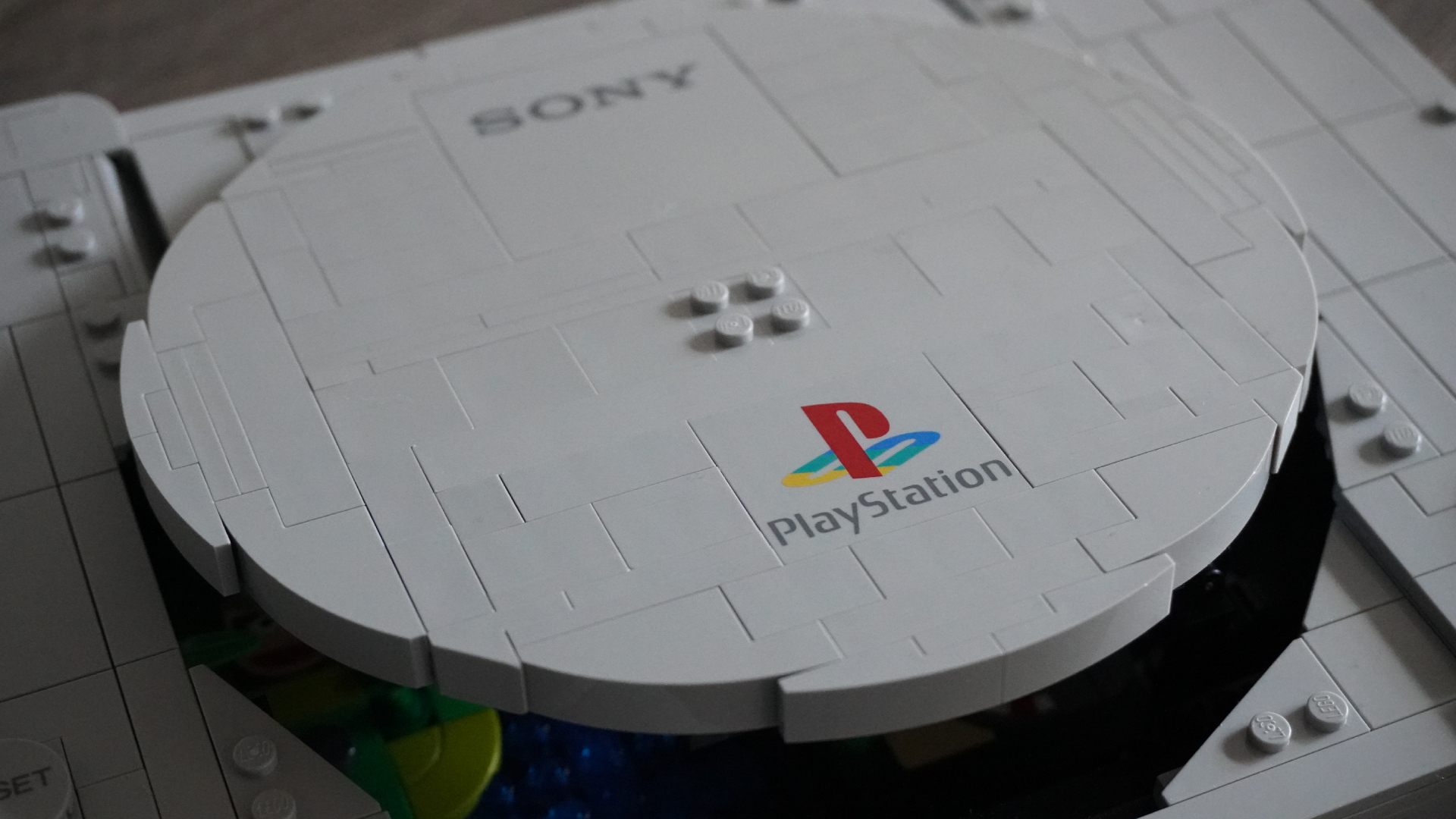 Close-up of a gray circular LEGO piece featuring the PlayStation logo and the word'PlayStation' printed on it, part of a larger LEGO model.