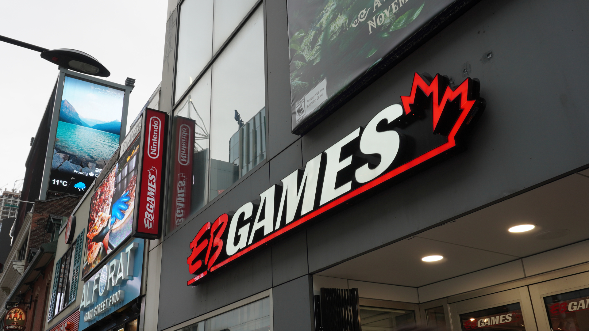Nintendo-Store-2 | iPhone in Canada Exterior view of an EB GAMES storefront with a bold white-and-red sign and red maple-crown logo on a dark facade.