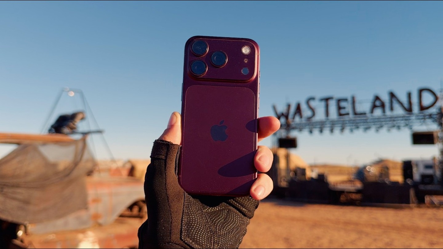 Burgundy iPhone 18 Pro held up in front of the Wasteland Weekend sign in the Mojave Desert